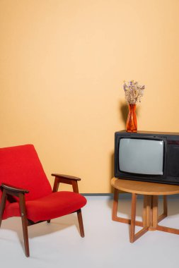 Armchair near tv and flowers on coffee table on orange background clipart