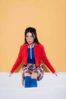 Havalı Asyalı kadın turuncu arka planda küvette poz veriyor.