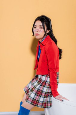 Havalı Asyalı model turuncu arka planda küvetin yanındaki kameraya bakıyor.