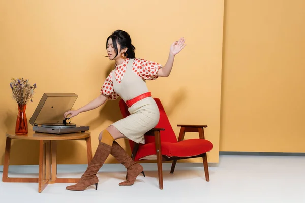 Giovane Donna Asiatica Utilizzando Giradischi Vicino Fiori Tavolino Sfondo Arancione — Foto Stock
