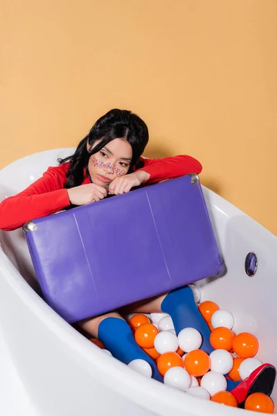 Pretty Asian Model Glitter Face Holding Retro Suitcase Bathtub Balls — Stock Photo, Image