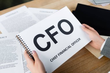 Ofisteki bulanık belgelerin yanında Cfo harfleriyle not defteri tutan iş kadını görüntüsü.