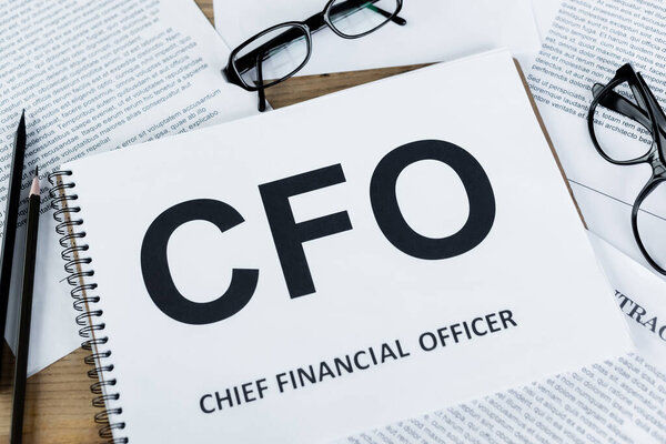top view of notebook with cfo abbreviation near documents and glasses on desk