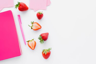 Yapışkan notların yanında olgun çileklerin üst görüntüsü ve beyaz arkaplanda pembe defter.