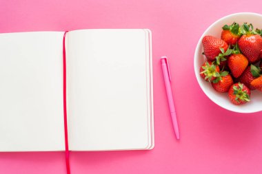 Pembe arka planda taze çilek ve kalem içeren açık defterin üst görünümü 