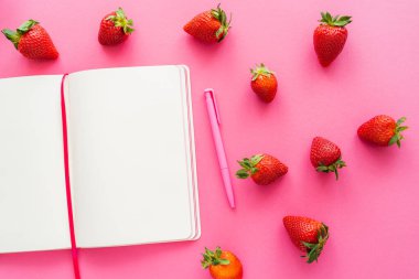 Organik çileklerin üst görüntüsü ve pembe arka planda açık bir defter. 