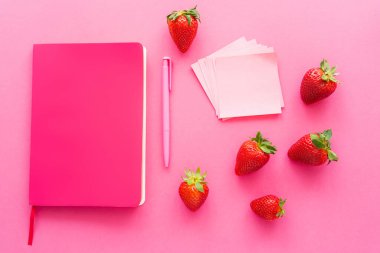 Olgun çileklerin yanındaki yapışkan notların üst görüntüsü ve pembe arka plandaki not defteri. 