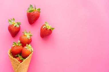 Pembe arka planda waffle külahında yaprakları olan çileklerin üst görüntüsü 