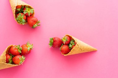 Pembe arka planda waffle külahları içinde taze çilekler. 