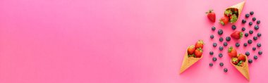 Waffle konilerinin yanında böğürtlenli, pembe arka planda çilekli, böğürtlenli bir daire. 
