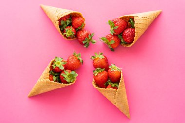 Pembe arka planda organik çilekler ve tatlı waffle külahlarıyla yatıyordu. 