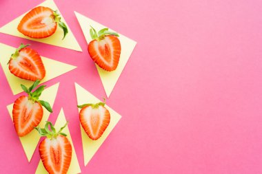 Dümdüz uzanmış pembe arka planda sarı üçgenler üzerinde sulu çileklerle