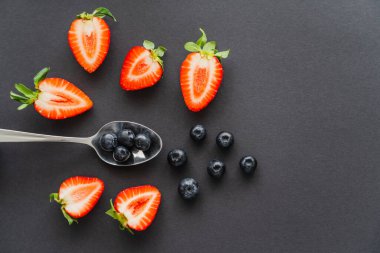 Siyah arka planda çileklerin yanında kaşıkta yaban mersinlerinin üst görüntüsü 