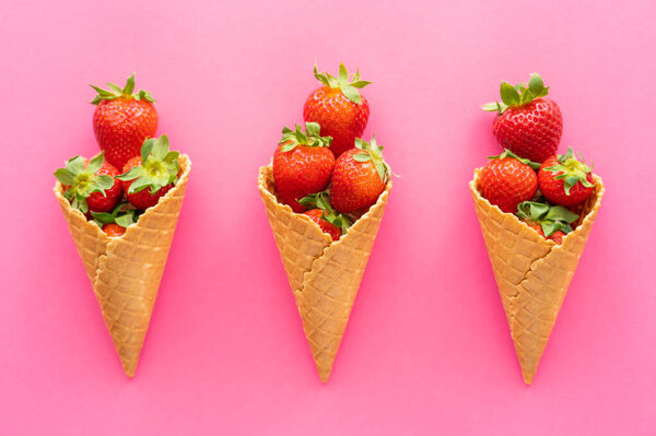 Flat lay with strawberries in waffle cones on pink background 