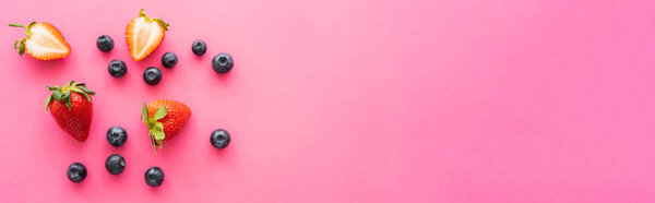 Вид сверху голубики рядом с разрезанной клубникой на розовом фоне, баннер 