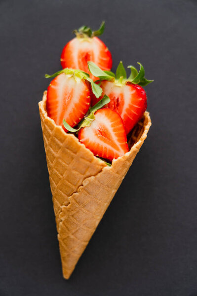 Top view of waffle cone with cut strawberries on black background 