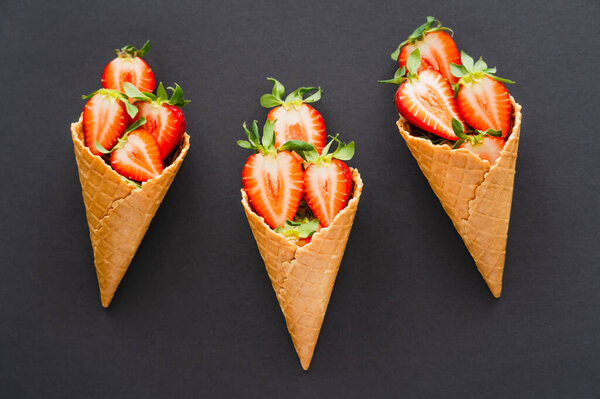Top view of ripe cut strawberries in waffle cones on black background 