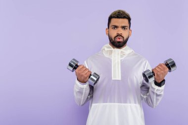Sakallı Afro-Amerikan sporcusu, mor üzerine izole edilmiş ağır dambıllarla egzersiz yapıyor. 