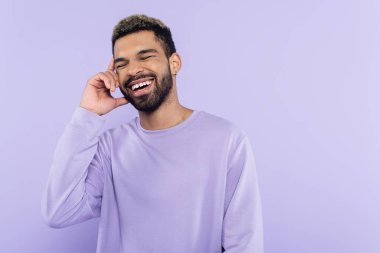 Mutlu Afro-Amerikan kazaklı adam akıllı telefondan konuşuyor ve mor üzerine izole bir şekilde gülüyor. 