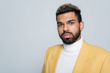 Sarı ceketli şık Afro-Amerikan adam gri renkli kameraya bakıyor.