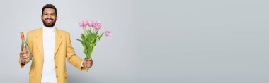 Gri pankartta izole edilmiş pembe lale buketi tutan şık kıyafetli Afro-Amerikan bir adam.