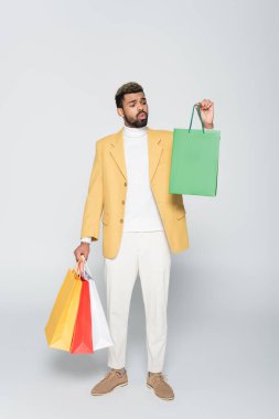 Sarı ceketli, polo yakalı ve gri üzerinde alışveriş torbaları taşıyan Afro-Amerikan bir adam. 