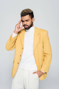 Düşünceli Afro-Amerikalı şık ceketli bir adam. Gri ceketin cebinde el ele poz veriyor. 