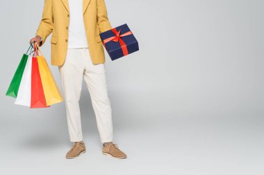 Sarı renkli ceketli Afro-Amerikan bir adamın hediye paketleri ve gri renkli alışveriş çantaları taşıdığını gördüm. 