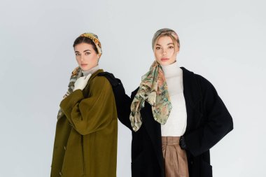 Eşarplı ve ceketli bir kadın el ele tutuşmuş, arkadaşının yanında, griye bürünmüş.