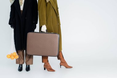 Gri arkaplanda portakallı çanta ve klasik bavul taşıyan kadınların kısmi görüntüsü