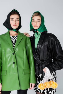 Ağ çantasında olgun portakallı bir kadın Gri renkli bir arkadaşın yanındaki kameraya bakıyor.