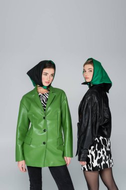 Gri üzerine izole edilmiş kameraya bakan deri ceketli ve mendilli şık kadınlar.