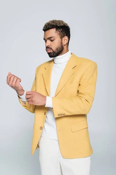 穿着黄色夹克的时髦的非洲裔美国人调整袖子 与灰色隔离 — 图库照片