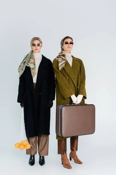 レトロなスーツケースとオレンジのネットバッグを着たファッショナブルな女性の完全な長さグレーの背景 — ストック写真
