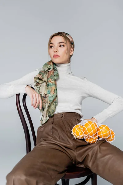 Trendy Woman Kerchief Sitting Chair Oranges Net Bag Isolated Grey — Stock Photo, Image