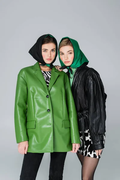 women in green and black jackets and kerchiefs looking at camera isolated on grey