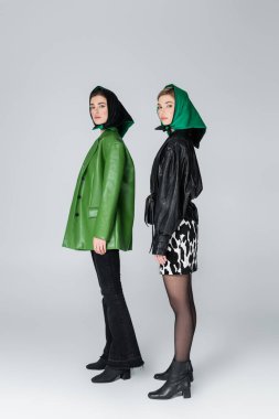 Gri arka planda duran şık giysili ve mendilli kadınların tam boy görünümü