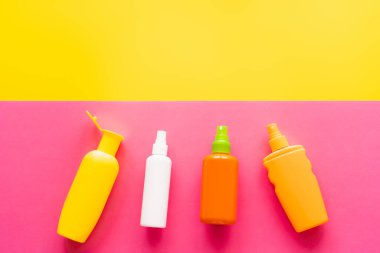 Sarı ve pembe arkaplanda güneş kremi şişelerinin üst görünümü 