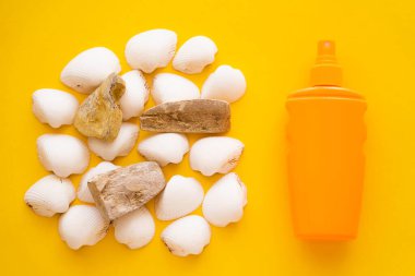 Top view of sunblock near white seashells on yellow background  clipart