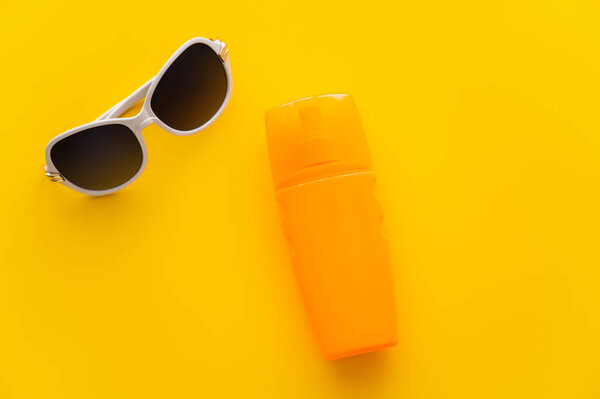Top view of sunglasses near sunscreen on yellow background 
