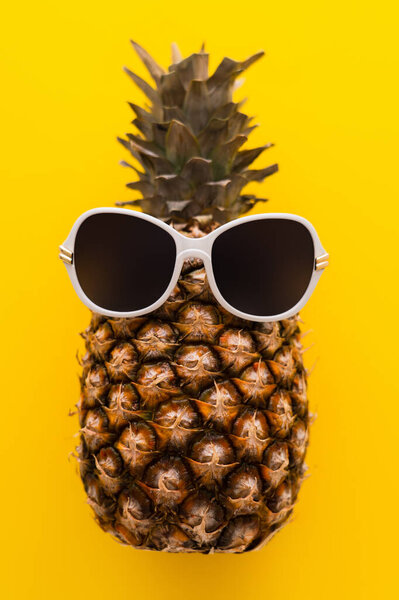 Top view of sunglasses on pineapple on yellow background 