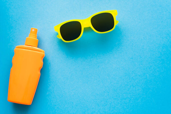 Top view of sunscreen and sunglasses on blue background 