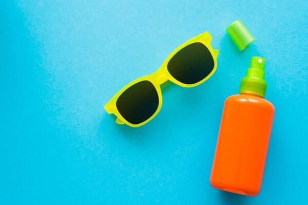 Top view of sunglasses near bottle of sunblock on blue background 