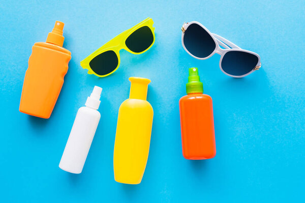 Top view of sunglasses and sunscreens on blue background 