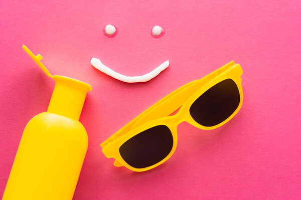Top view of smile sign from sunscreen near bottle and sunglasses on pink background 