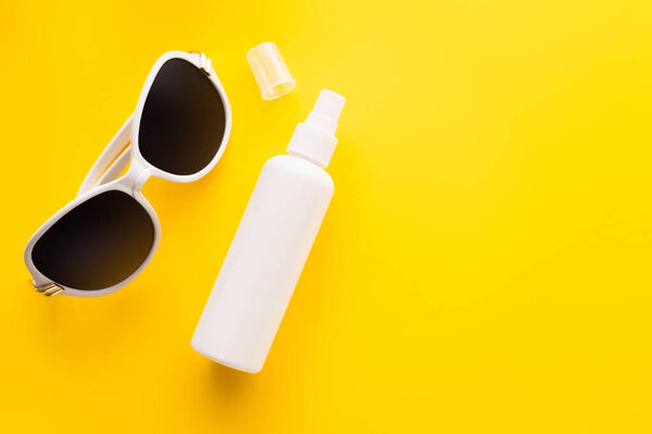 Top view of sunglasses near sunblock in bottle on yellow surface 