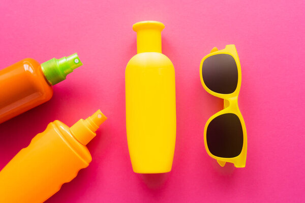 Top view of sunglasses near sunscreen bottles on pink surface 
