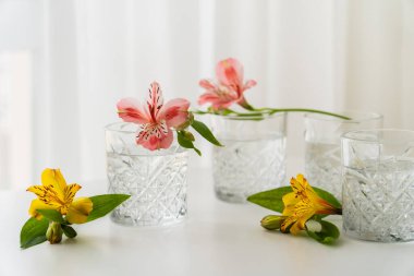 Sarı ve pembe alstromerya çiçekleri beyaz masa üstünde suyla bardakların yanında. 