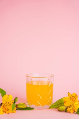 glass of fresh citrus juice and yellow tropical flowers on pink background clipart
