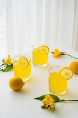 Beyaz masa üstünde Alstroemeria 'nın yanında sulu limon dilimleri ile bir bardak limonata.